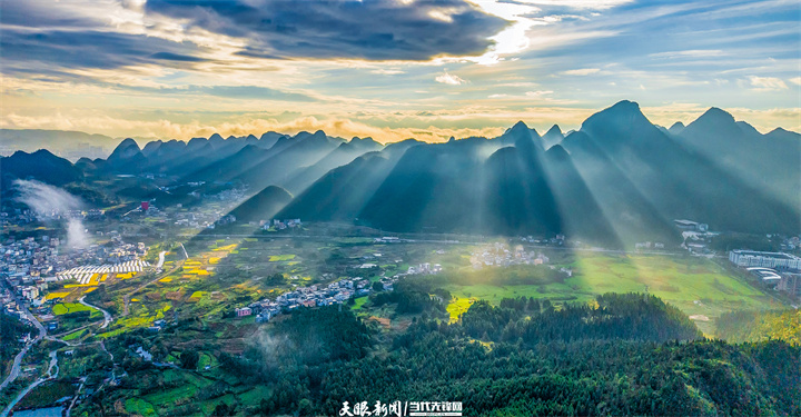 黔西南州兴义市万峰林景区，老袜山日出时分霞光漫洒，光束映田园村寨如绘卷铺展。.jpg